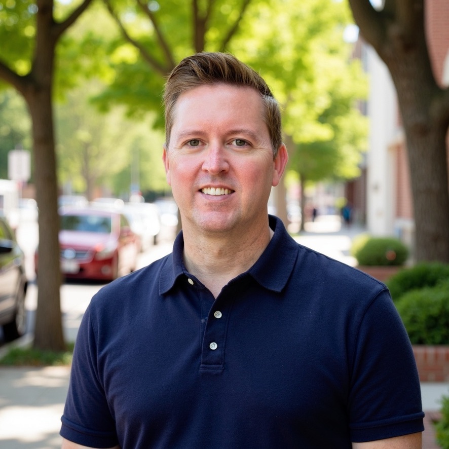 Patrick Gibson in a navy polo outdoors on a tree-lined street